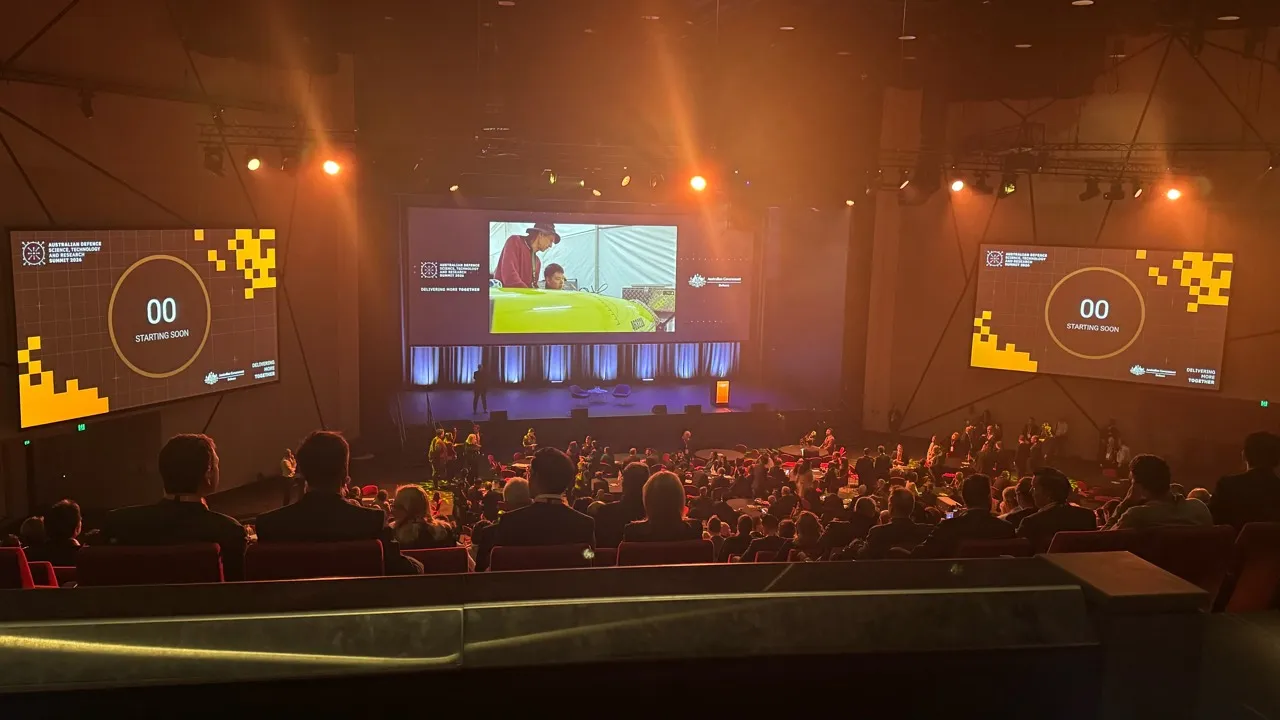 Delegates in the auditorium facing presentation screens displaying ADSTAR Summit 2026 signage.